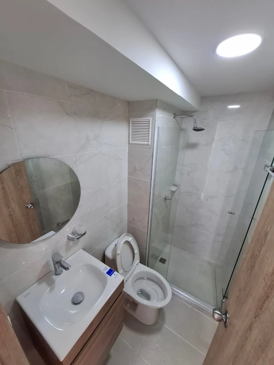 Baño con ducha en vidrio y espejo circular